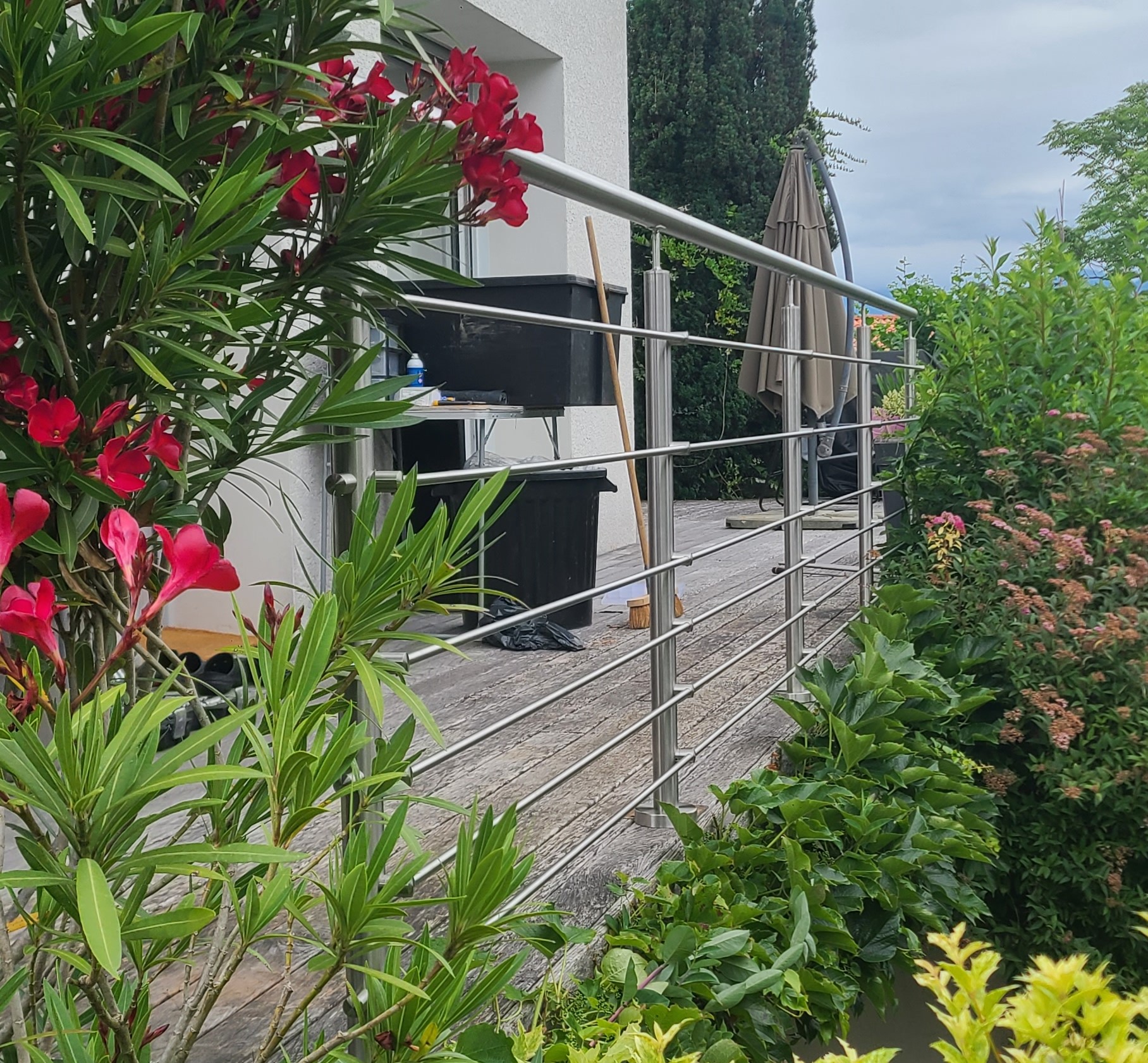 Garde-corps en inox installé sur une terrasse en bois entourée de végétation
