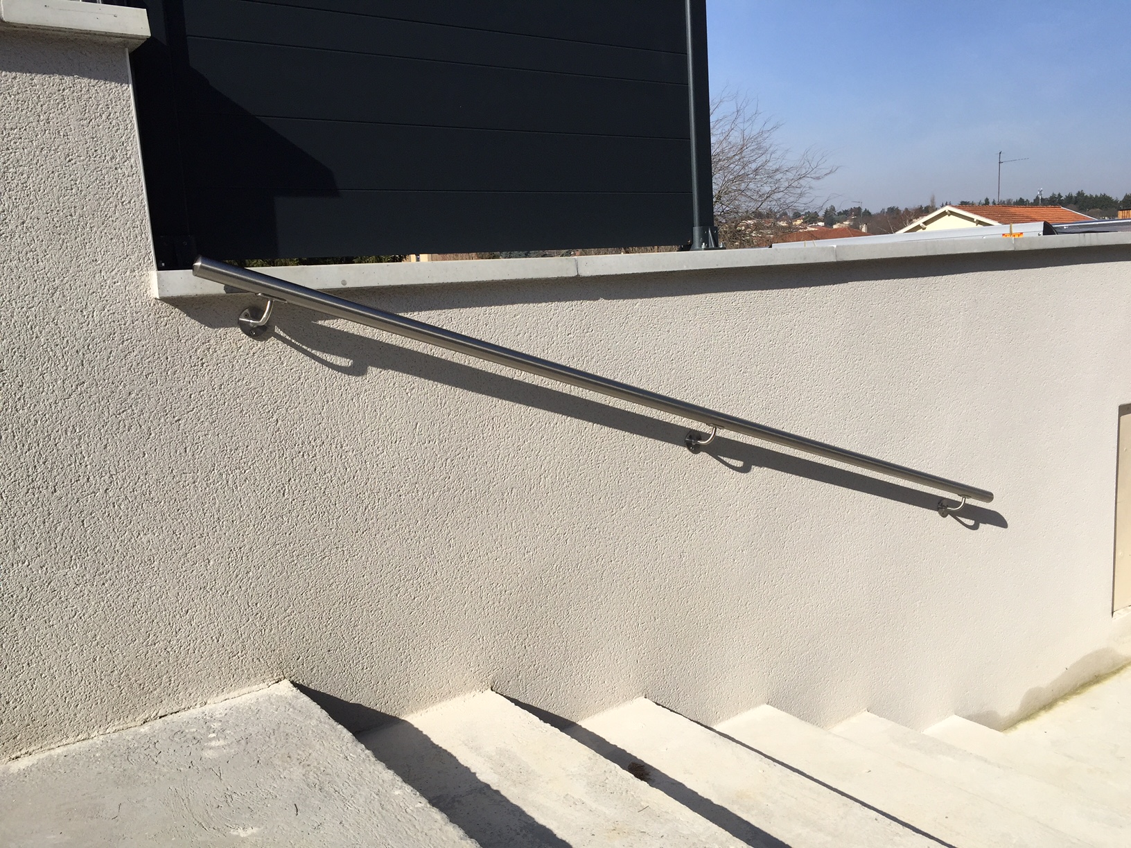 Main courante inox pour escalier extérieur Main courante inox fixée sur trois supports muraux le long d’un escalier extérieur bordé d’un mur enduit clair.