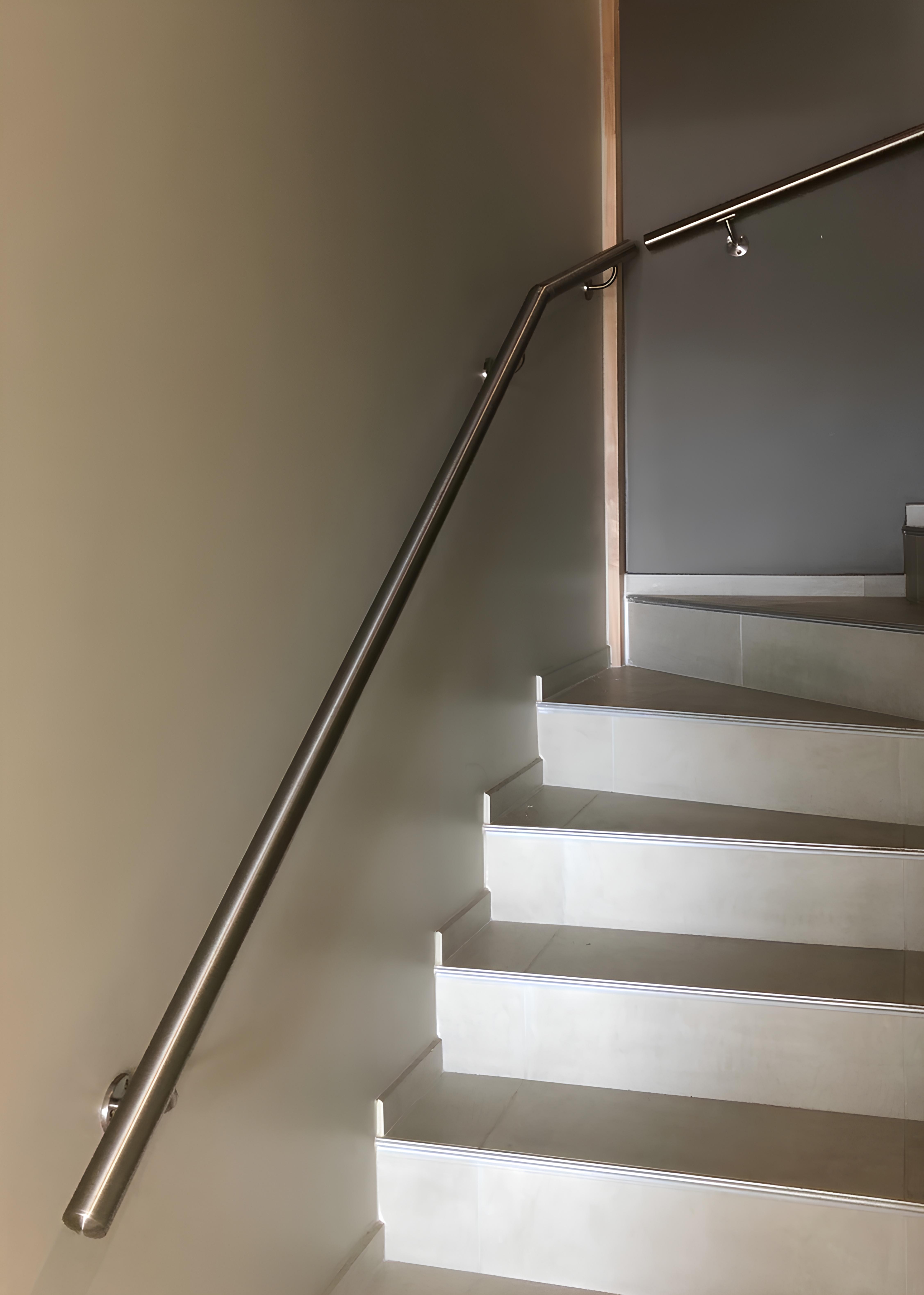 Main courante inox coudée pour escalier tournant Main courante inox murale avec coude suivant un escalier intérieur tournant aux marches carrelées claires.
