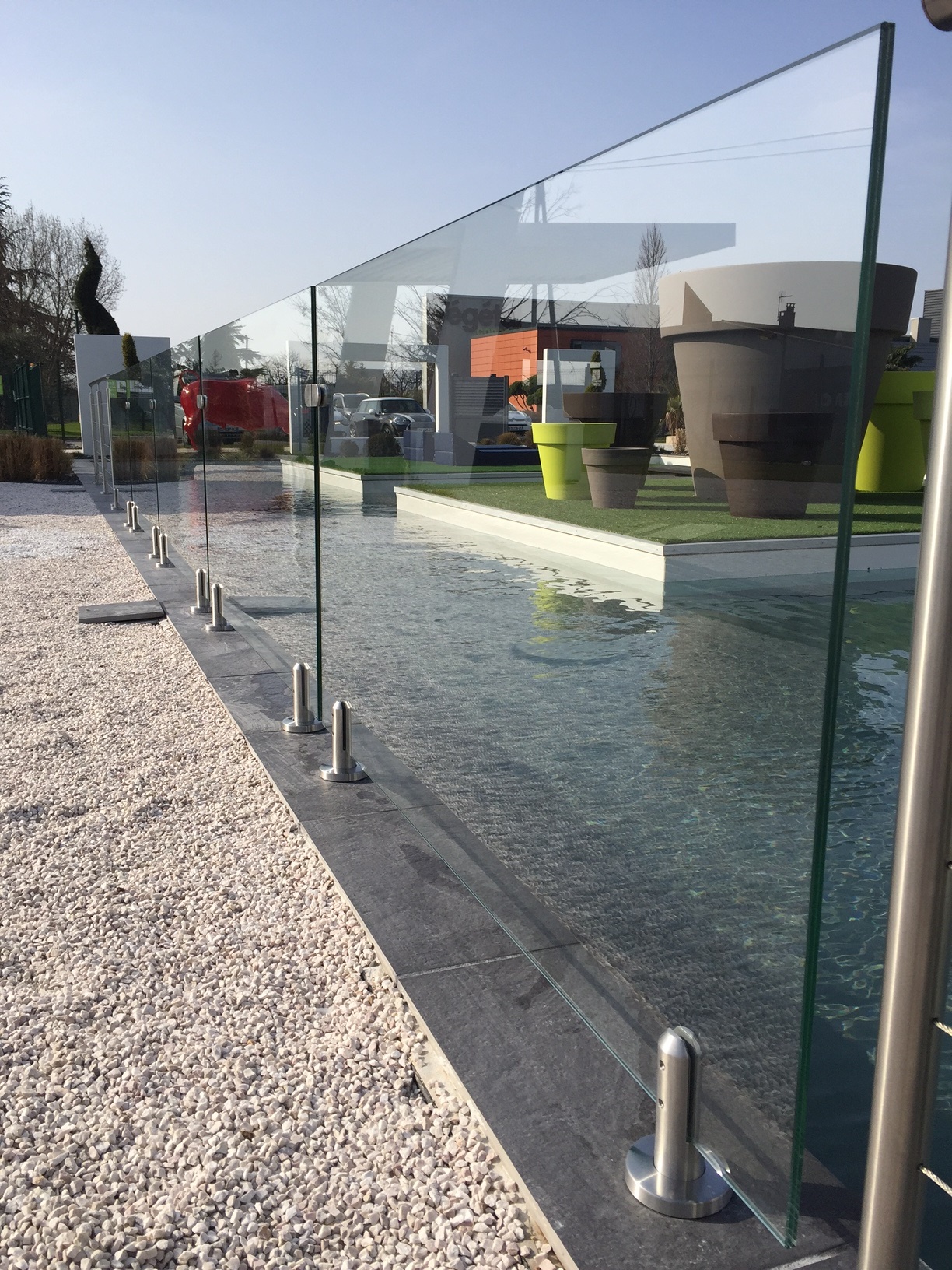 Panneaux de verre maintenus par des pinces rondes inox au sol en bordure de piscine