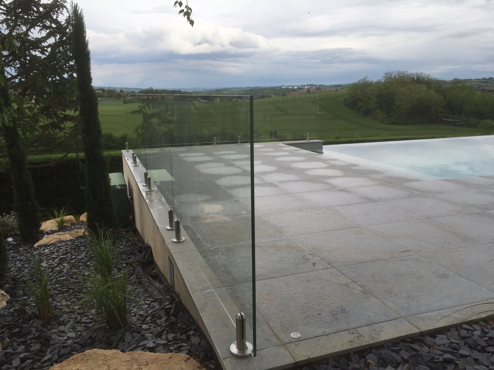 Garde-corps en verre avec pinces inox au sol autour d’une piscine Garde-corps en verre feuilleté 44/2 installé autour d’une piscine sur terrasse carrelée, avec pinces inox au sol, résistant en extérieur.