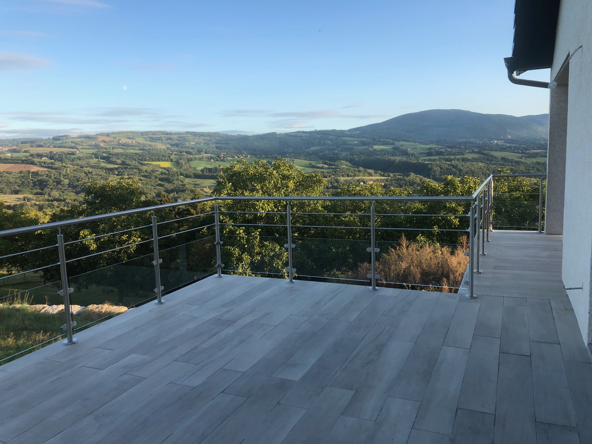 Vue d’une balustrade en verre et lisses inox pour balcon, au design moderne. Balustrade en verre et lisses inox installée sur un balcon, résistante en extérieur, sur poteaux inox, avec pinces inox et au design moderne