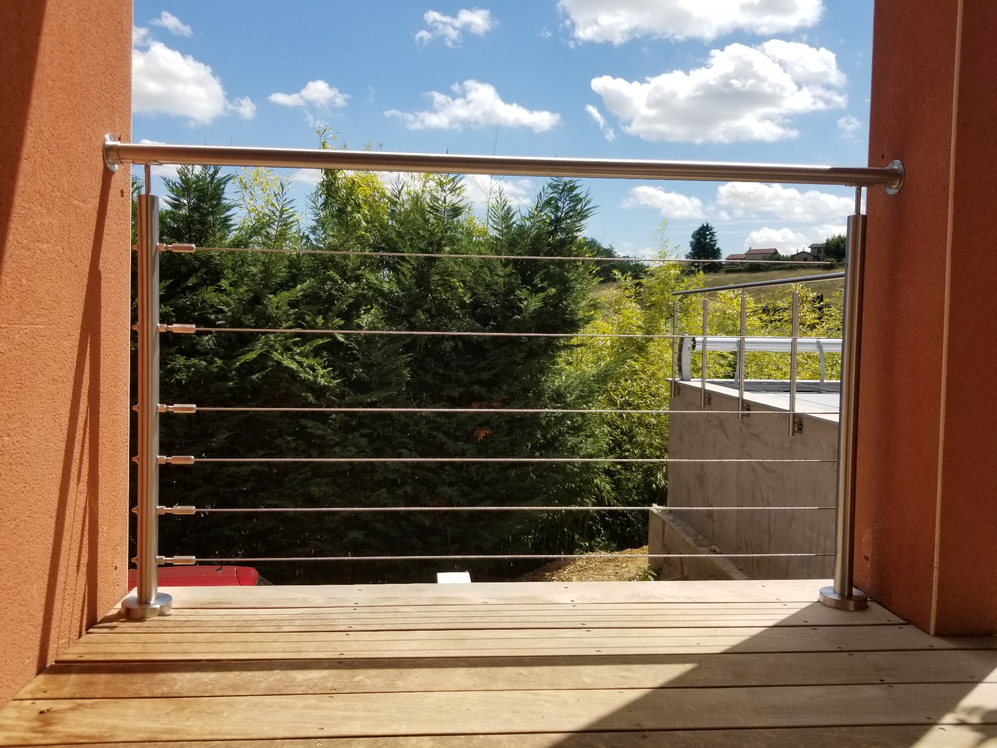 Détail d’un garde-corps en inox à câbles pour terrasse bois avec fixation murale, équipé de tendeurs de câbles. Garde-corps fabriqué en inox 316 à câbles pour terrasse bois avec fixation murale, avec tendeurs de câbles