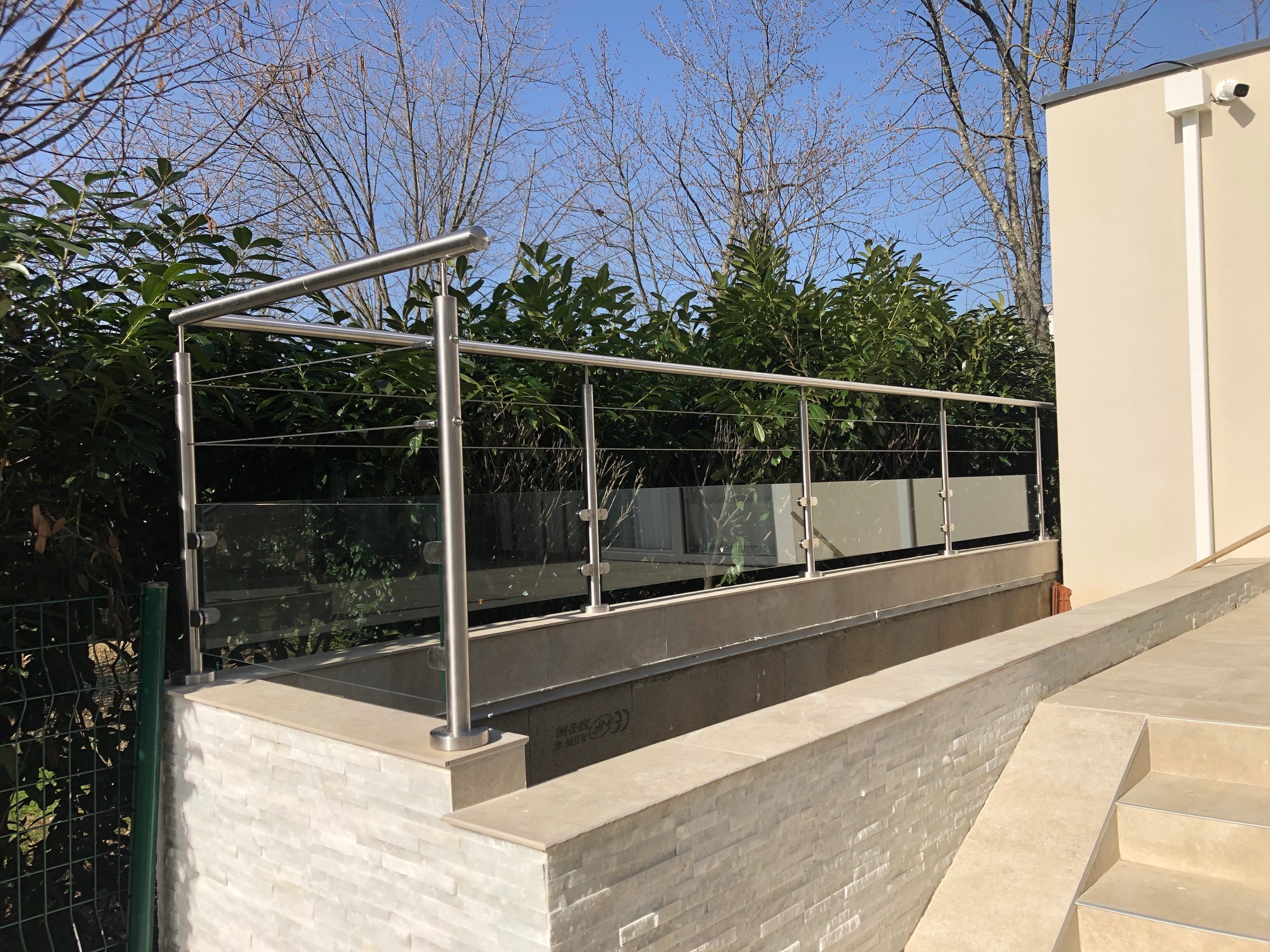 Vue d’un garde-corps en verre 44/2 et câbles inox sur acrotère avec support carrelé. Fabrication d’un garde-corps en verre 44/2 et câbles en inox 304 tendus sur acrotère avec support carrelé, sur montants inox