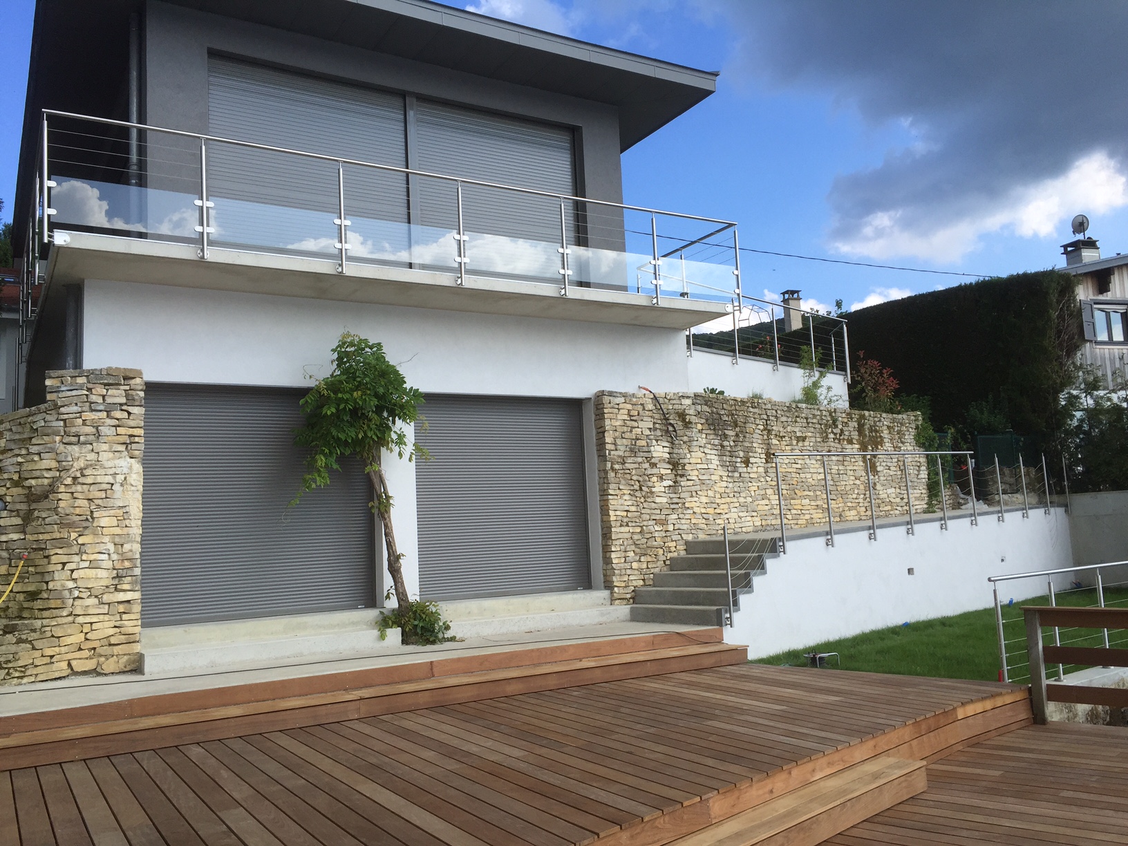 Aperçu d’un garde-corps en verre et câbles inox pour balcon avec pose à l’anglaise, avec barre inox. Garde-corps en verre feuilleté 44/2 et câbles inox posé sur un balcon, avec platine de fixation latérale et barre inox et au design moderne