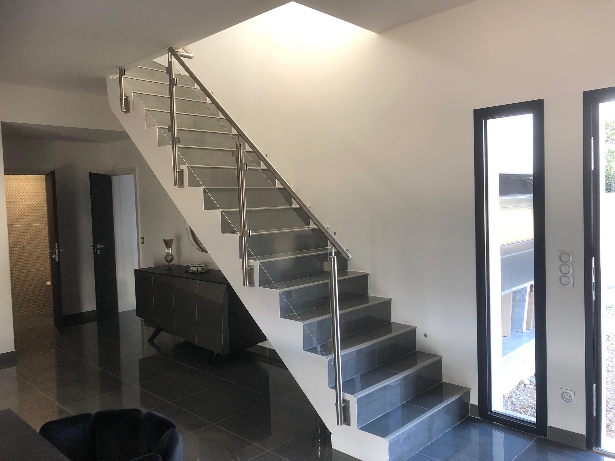 Aperçu d’un garde-corps en verre pour escalier intérieur avec pose à l’anglaise, au design moderne. Garde-corps en verre trempé installé le long d’un escalier intérieur, avec platine de fixation latérale et structure en tube inox et au design moderne