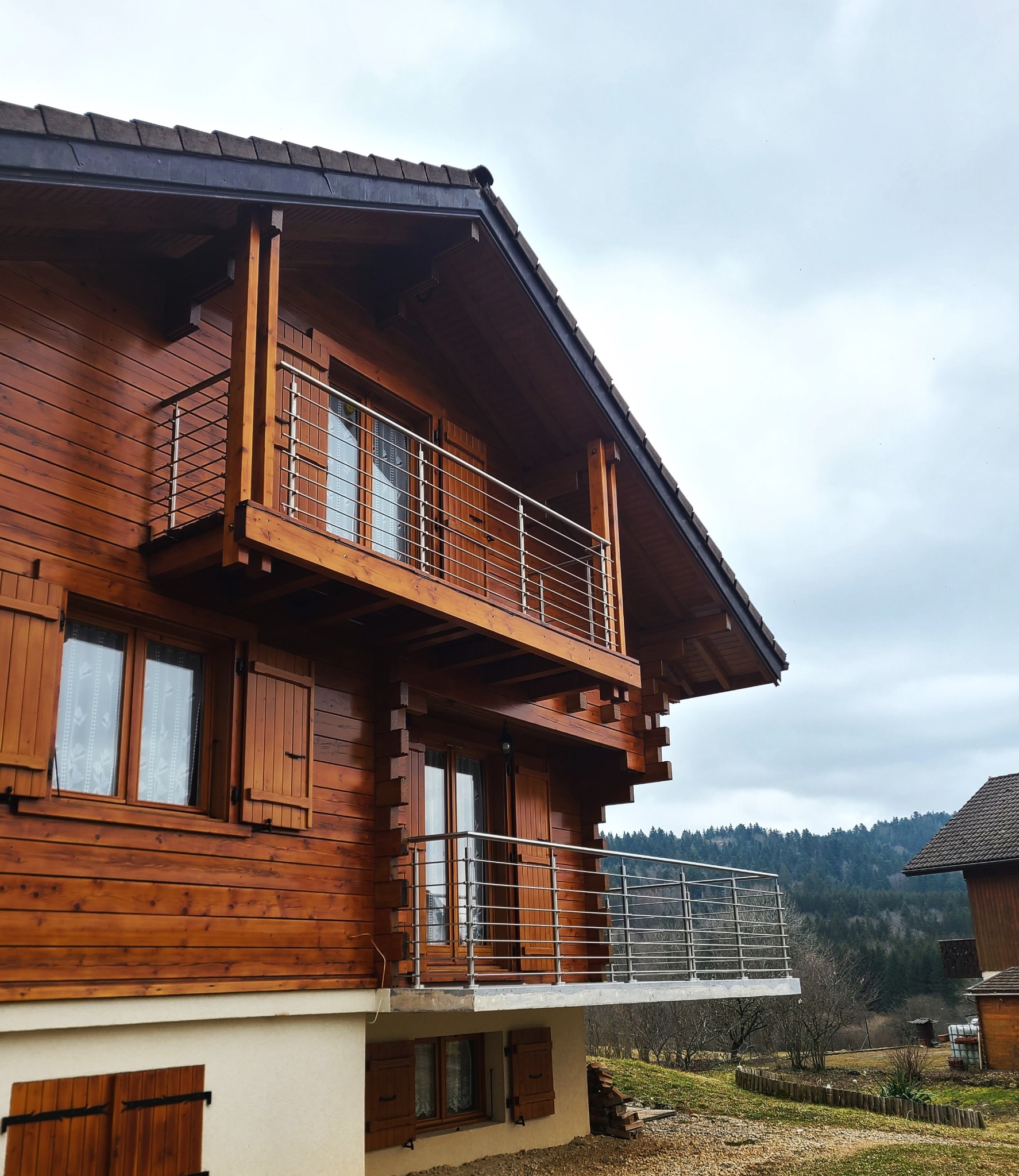 Aperçu d’une rambarde en inox à 6 lisses pour balcon de chalet en bois, avec montants inox. Rambarde en inox brossé à 6 lisses posée sur un balcon de chalet en bois, sur montants inox et platine de pose au sol et avec tubes inox horizontaux