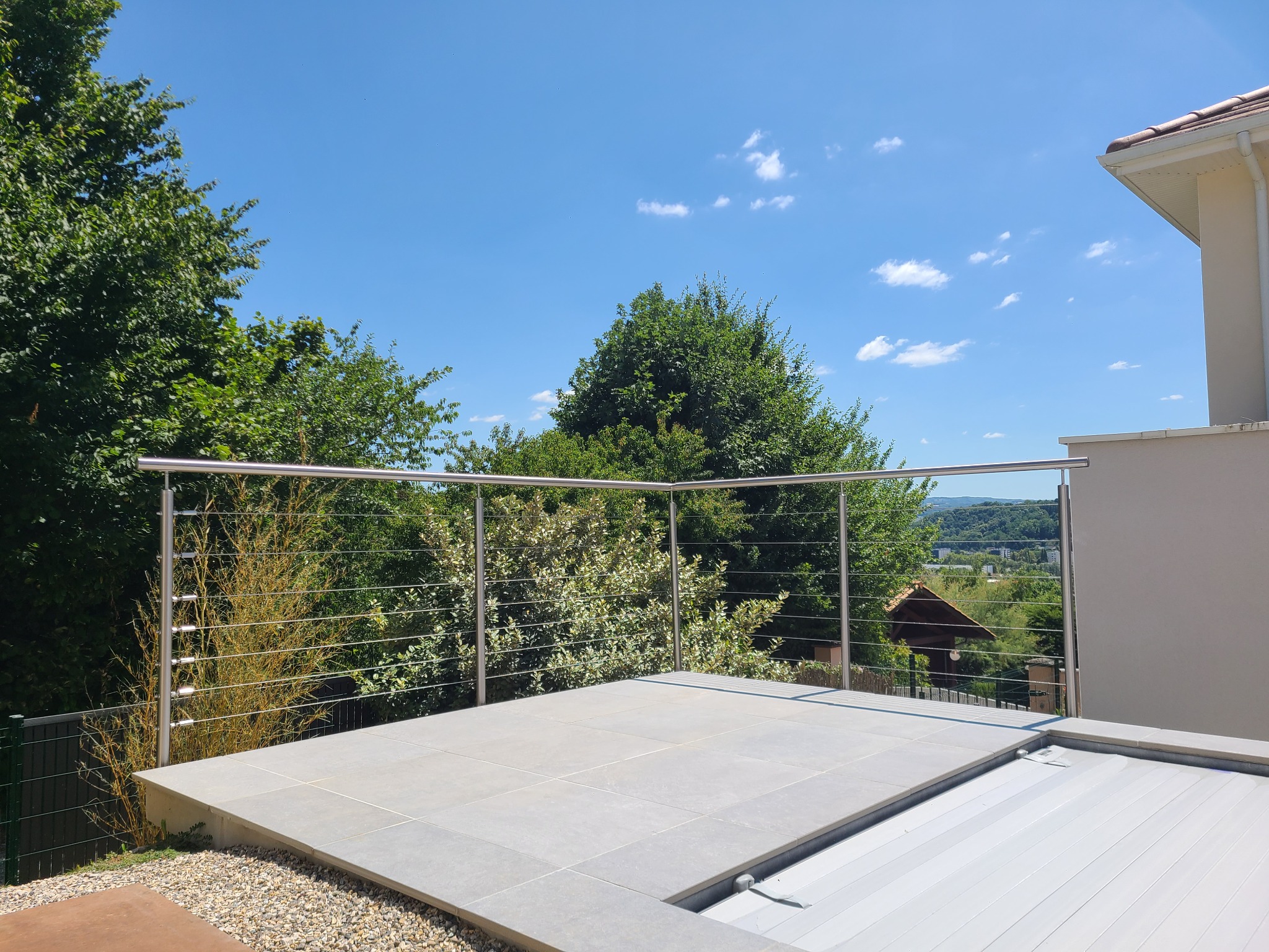 Vue d’une rambarde en inox brossé à câbles pour piscine avec fixation latérale. Rambarde installée en inox brossé à câbles tendus aux abords de piscine, posée en applique et résistante au chlore