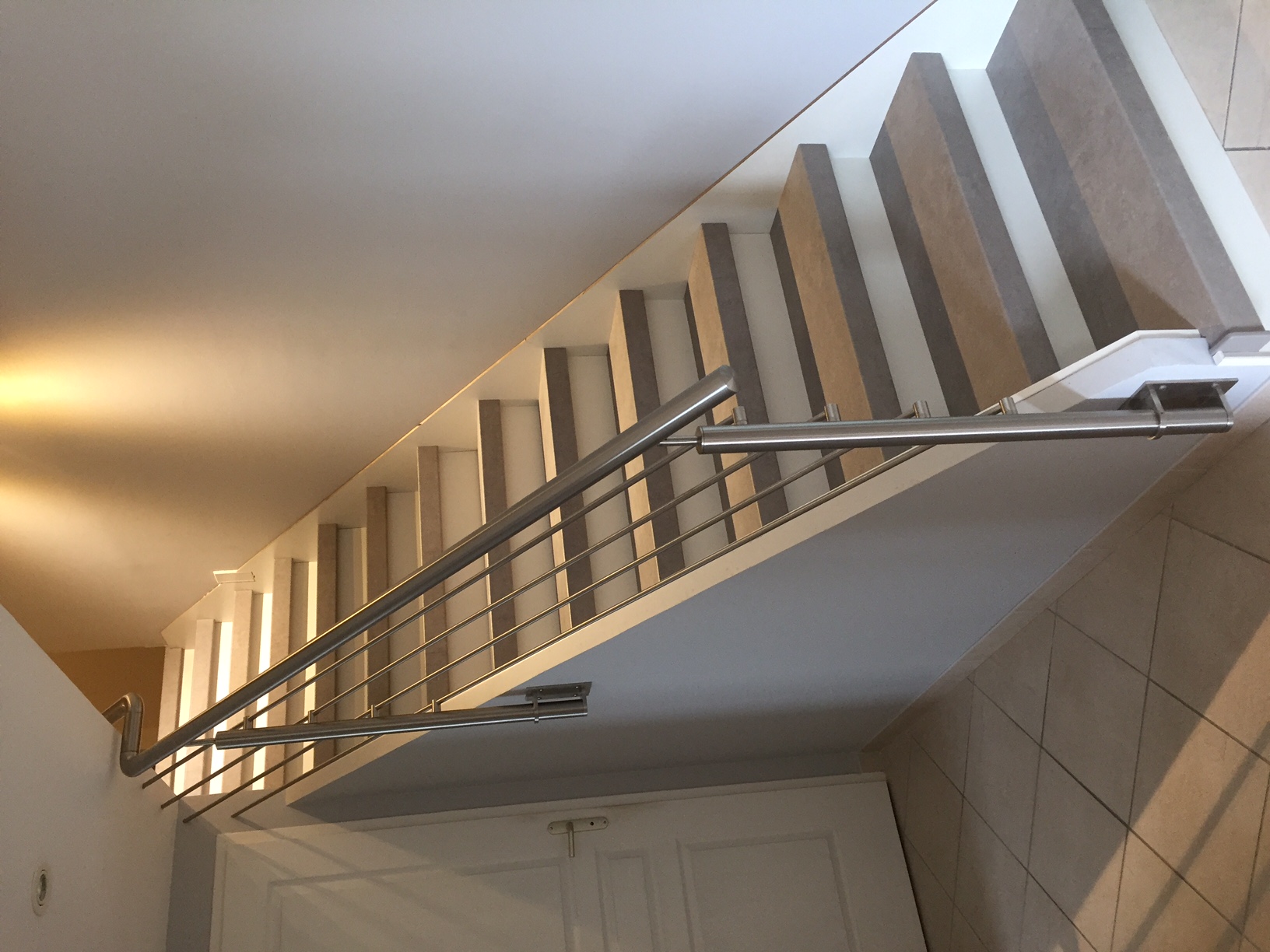 Vue d’une rambarde en inox à lisses pour escalier intérieur avec fixation latérale, au design moderne. Rambarde en inox à lisses installée le long d’un escalier intérieur, en pose à l’anglaise, avec remplissage à lisses et au design moderne