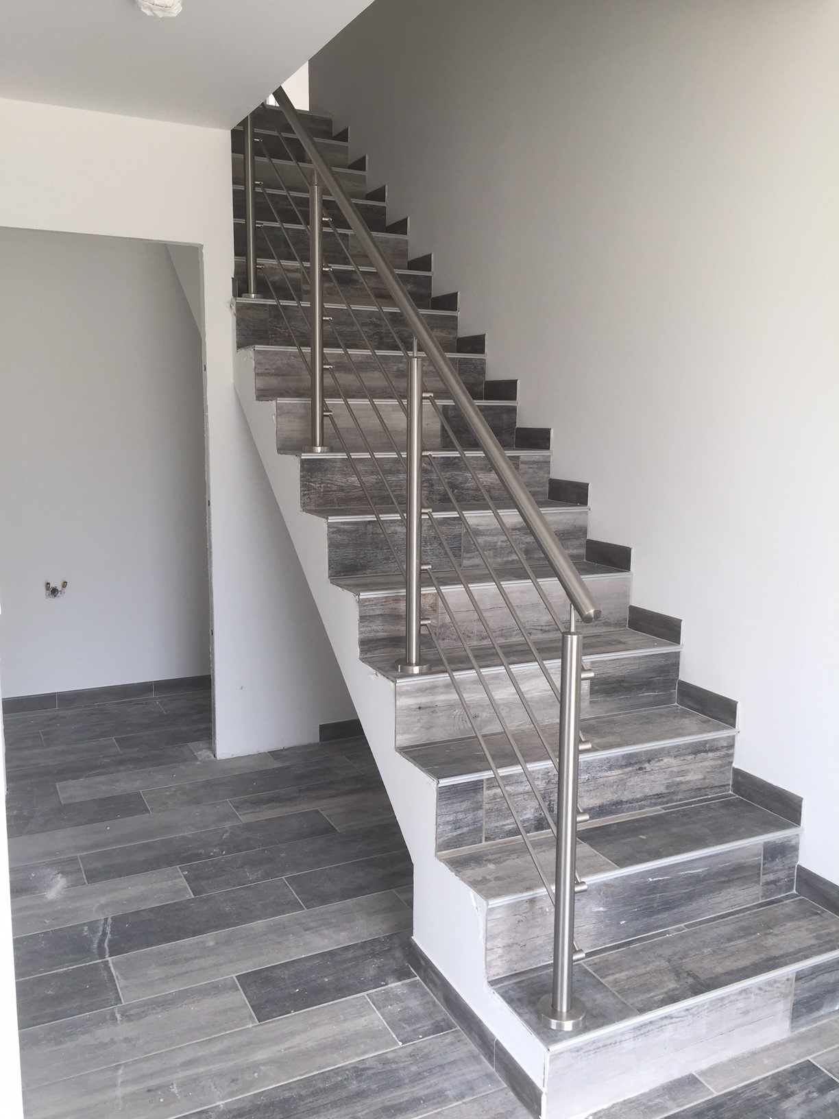 Détail d’une rambarde en inox à lisses pour escalier intérieur, montée sur platine de pose au sol. Rambarde en inox brossé à lisses horizontales posée le long d’un escalier intérieur, sur platine de pose au sol et avec structure en tube inox