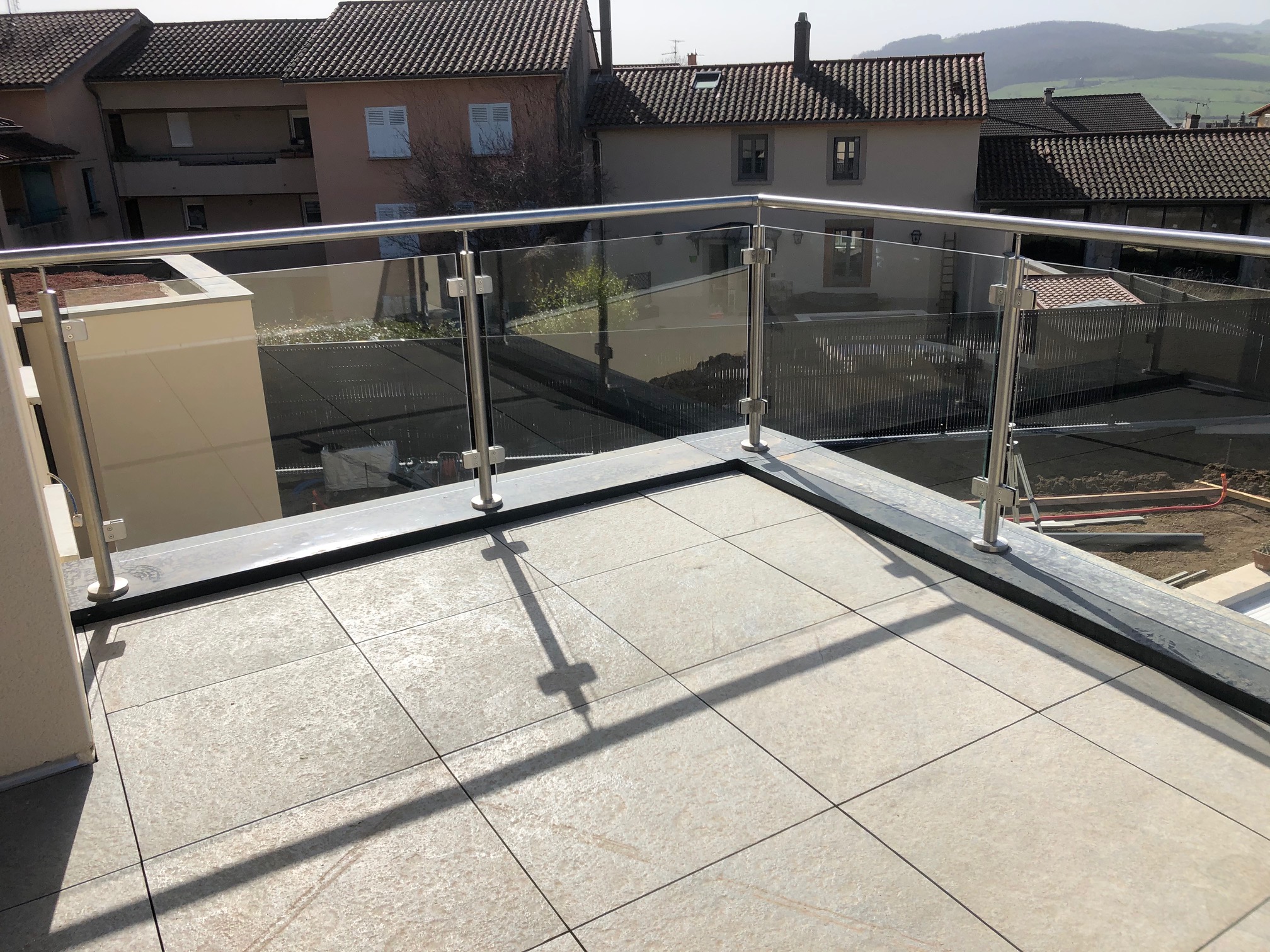 Détail d’une rambarde en verre sur acrotère avec couvertine aluminium RAL 7016, avec remplissage en verre. Rambarde fabriquée en verre feuilleté 44/2 sur acrotère avec couvertine aluminium RAL 7016, avec pinces à verre et remplissage verre