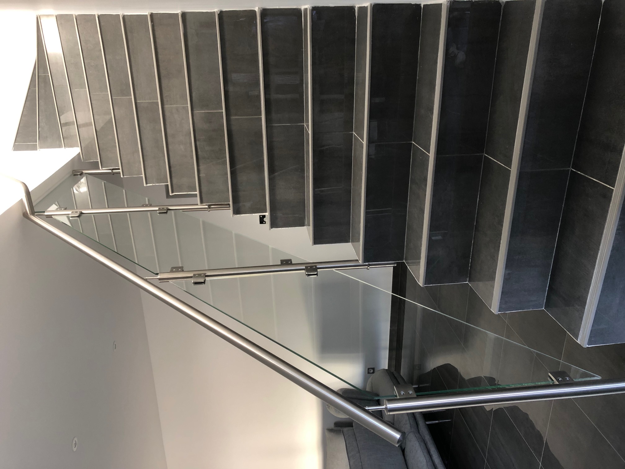 Vue d’une rambarde en verre pour escalier intérieur avec fixation latérale, fixée par pinces inox. Fabrication d’une rambarde en verre trempé 8,76 mm pour escalier, posée en applique et avec pinces inox