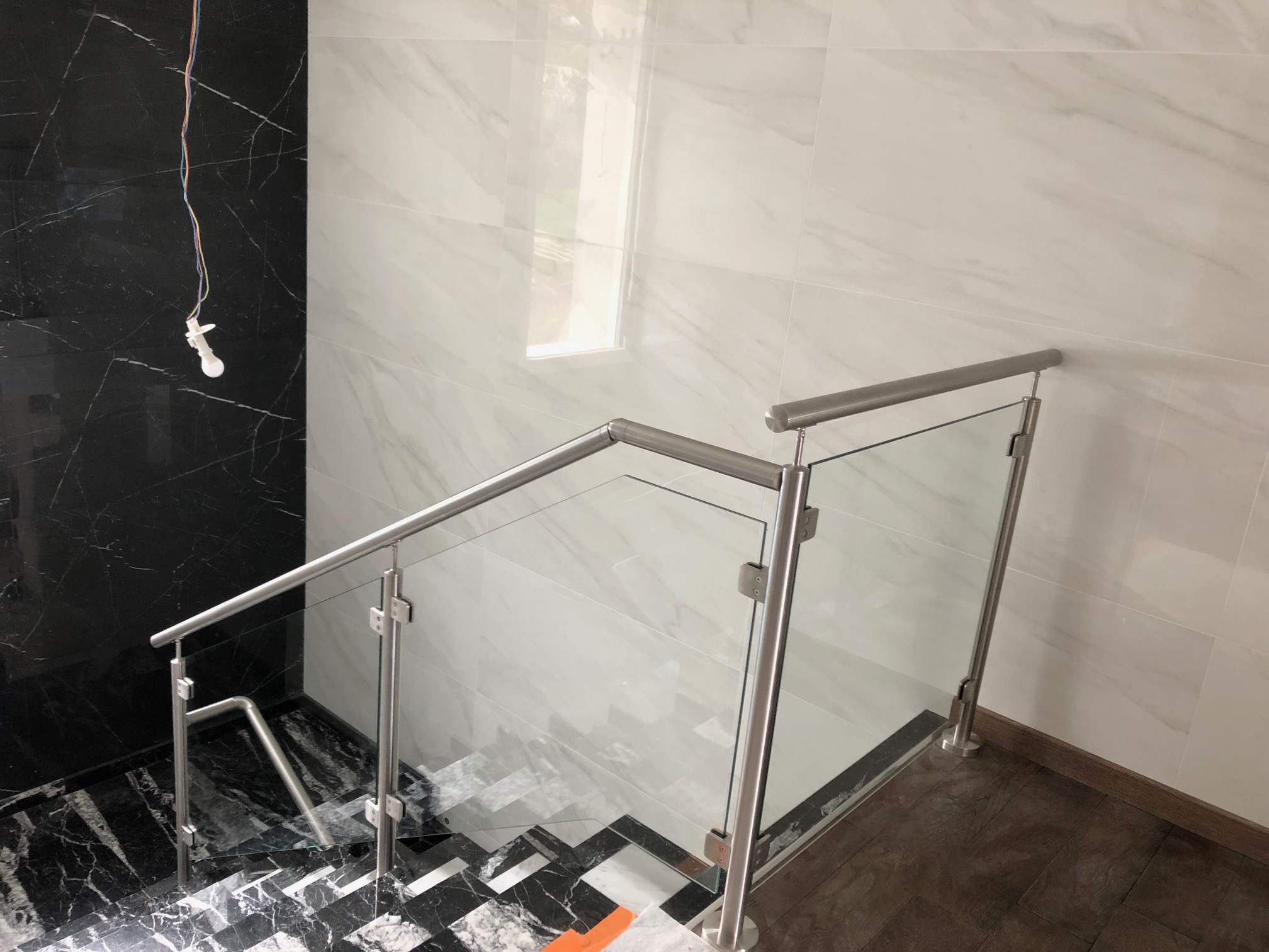 Détail d’une rambarde en verre pour escalier intérieur en marbre, avec remplissage en verre. Rambarde en verre feuilleté 44/2 pour escalier intérieur en marbre, en pose à la française et avec pinces à verre et remplissage verre