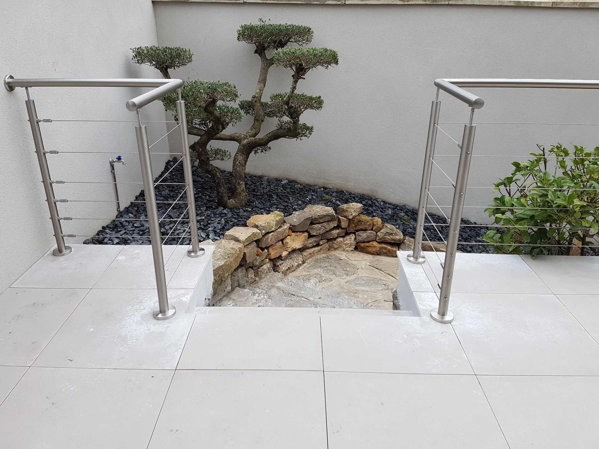 Aperçu d’une rampe d’escalier en inox à câbles pour terrasse carrelée, fixée sur embase de fixation horizontale. Rampe d’escalier en inox 304 à câbles installée sur une terrasse carrelée, sur embase de fixation horizontale et avec structure sur poteaux
