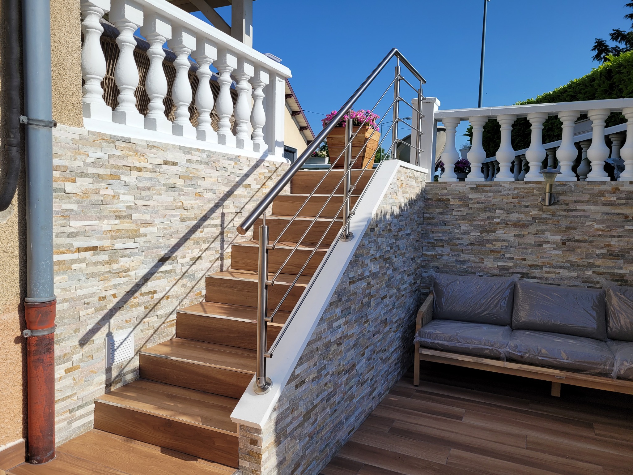 Vue d’une rampe d’escalier en inox à lisses sur limon avec pose à la française, prévue pour l’extérieur. Rampe d’escalier en inox à lisses installée sur limon avec pose à la française, en extérieur et avec barre inox